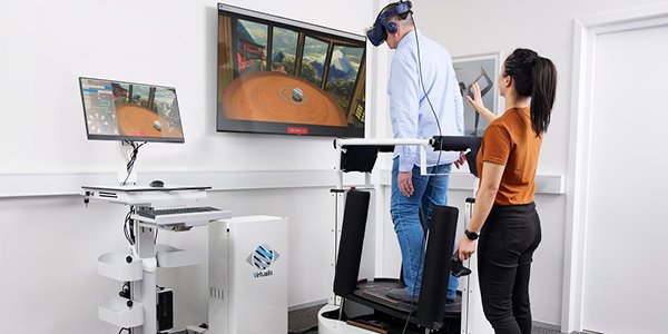 En audiolog/fysioterapeut hjælper en klient med BalanceVR-udstyr i en balance- og rehabiliteringsøvelse på MotionVR-platformen