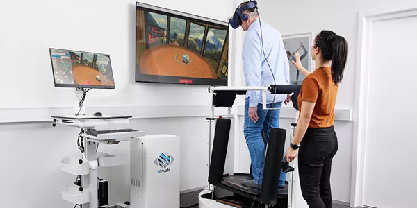 En audiolog/fysioterapeut hjælper en klient med BalanceVR-udstyr i en balance- og rehabiliteringsøvelse på MotionVR-platformen