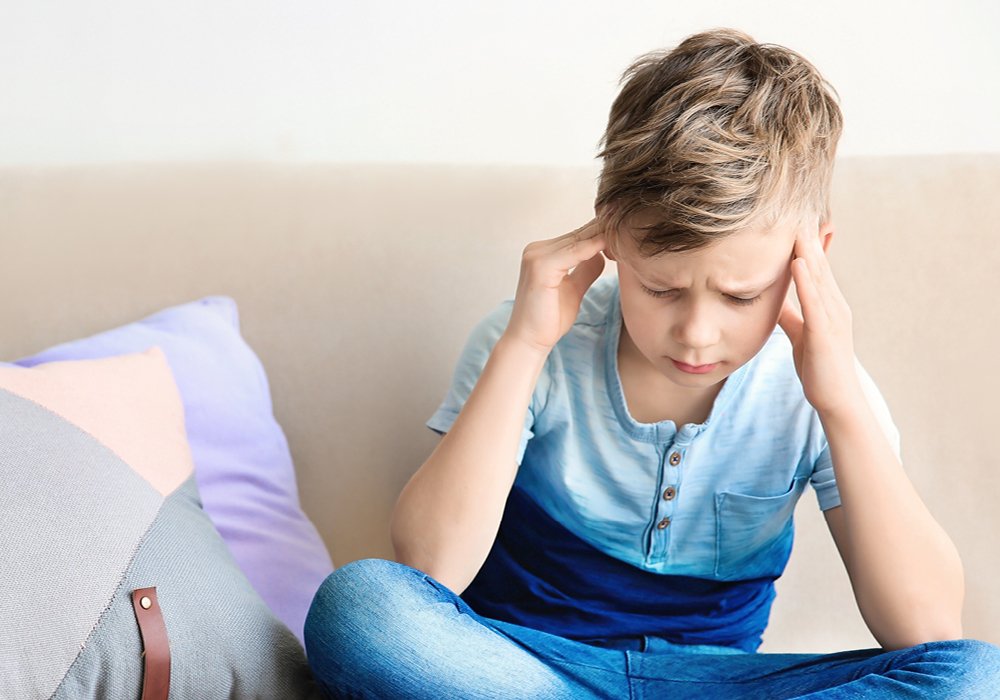 Barn sidder i sofa og tager sig til hovedet med rynkede øjenbryn 