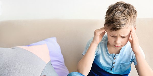 Barn sidder i sofa og tager sig til hovedet med rynkede øjenbryn 