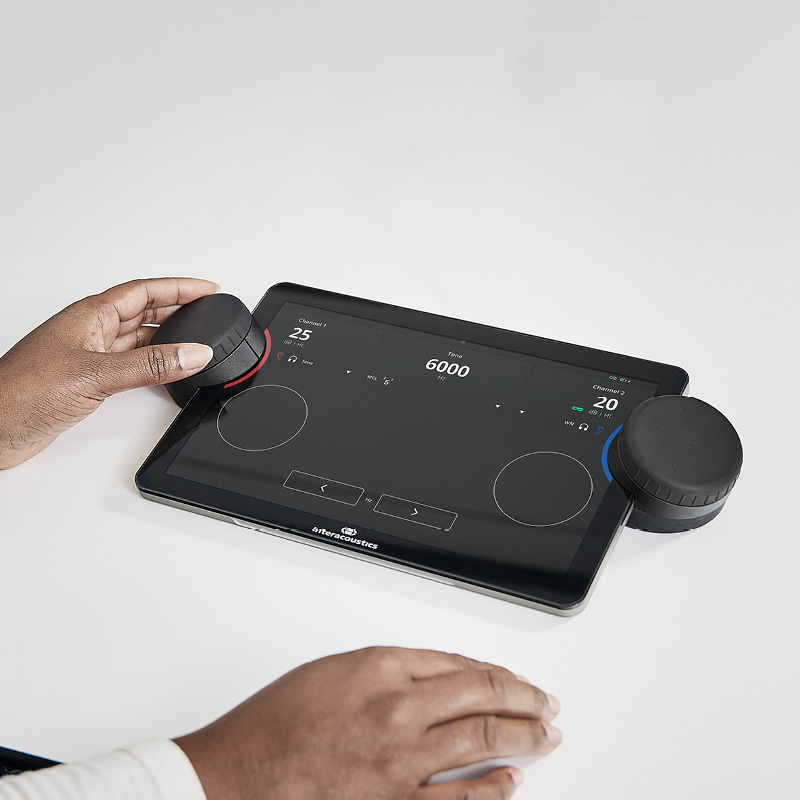 The Interacoustics Touch Keyboard is sitting on a desk, and an audiologist is navigating it using the left dial