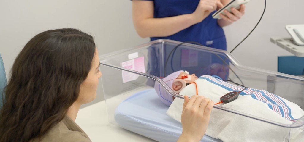 A nurse performing AABR testing on an infant in a bassinet 