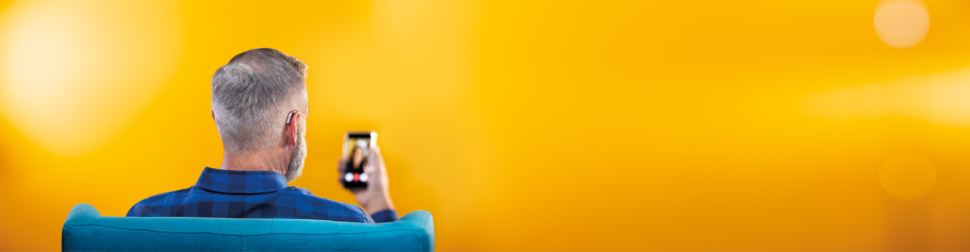 Middle-aged man using his smartphone and his Philips HearLink hearing aids to connect to friends by making a video call.