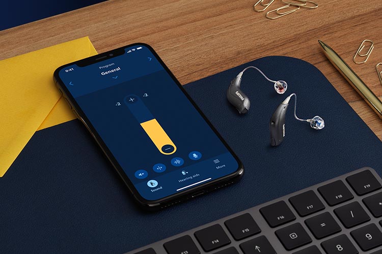 Philips HearLink miniRITE T R hearing aids next to a smartphone with the Philips HearLink app 2 open. 