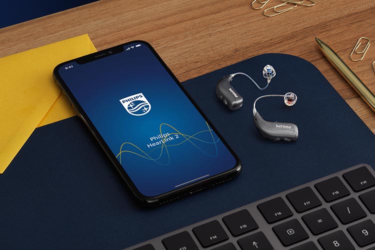 Philips HearLink miniRITE T R hearing aids next to a smartphone with the Philips HearLink app 2 open. 