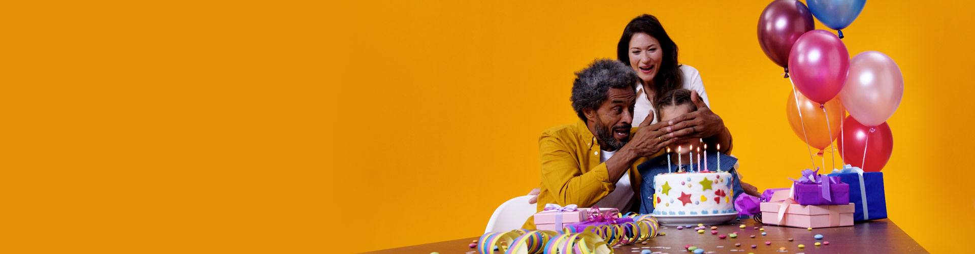 Grandfather with Philips HearLink hearing aids and his daughter celebrate his granddaughter's birthday with cake, balloons and gifts.