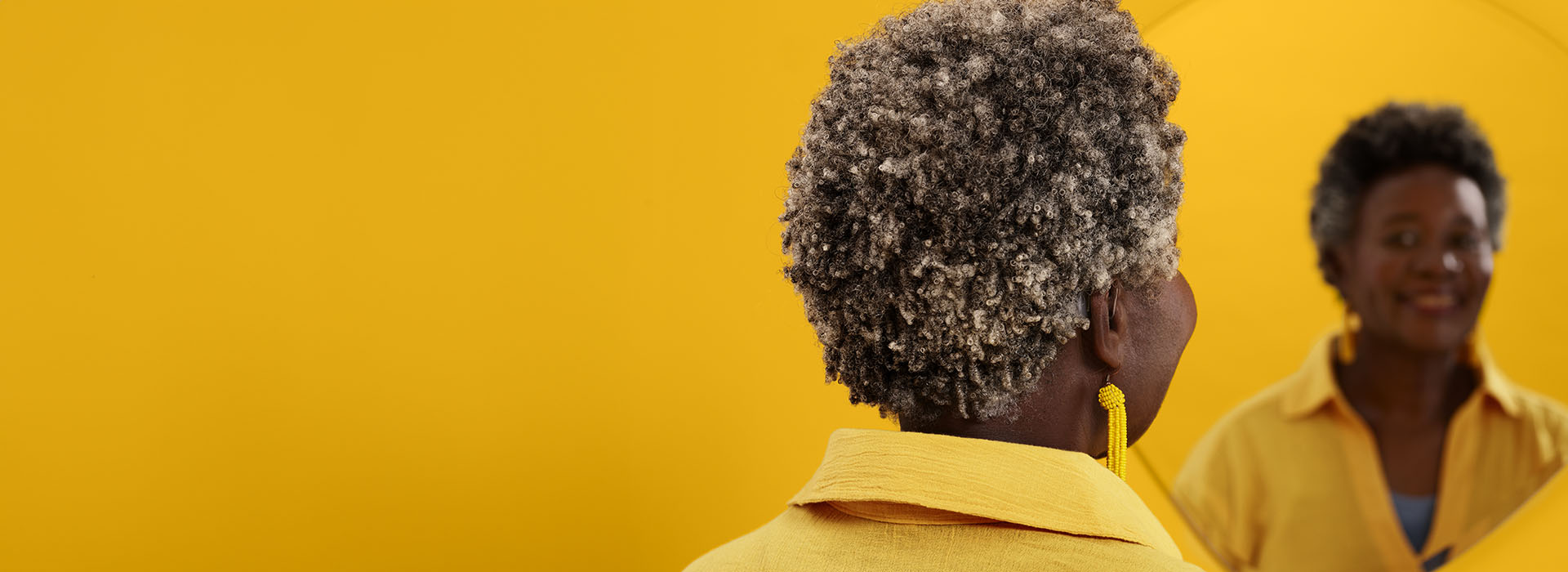 A granddaughter holds a teddy bear while sitting on the back of her grandfather who wears Philips HearLink hearing aids. Her mother also reaches out to hold her daughter.