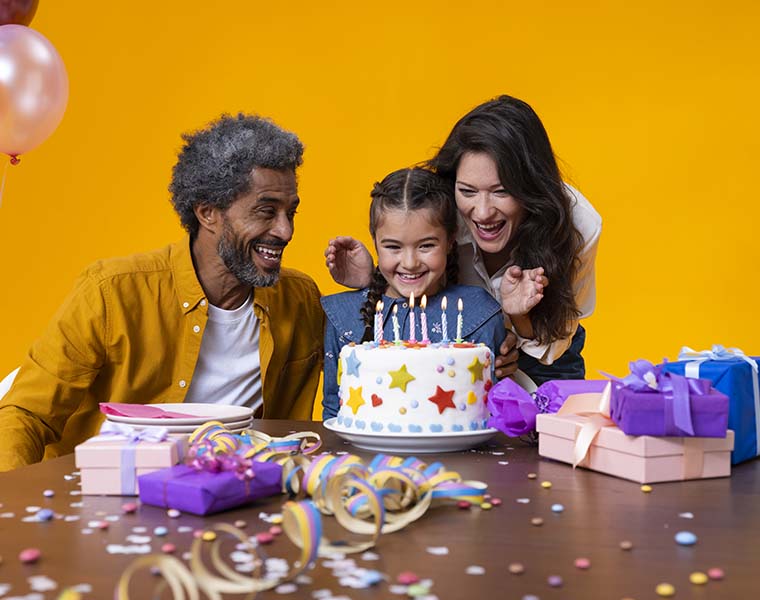 Grandfather with Philips HearLink hearing aids and his daughter celebrate his granddaughter's birthday with cake, balloons and gifts.