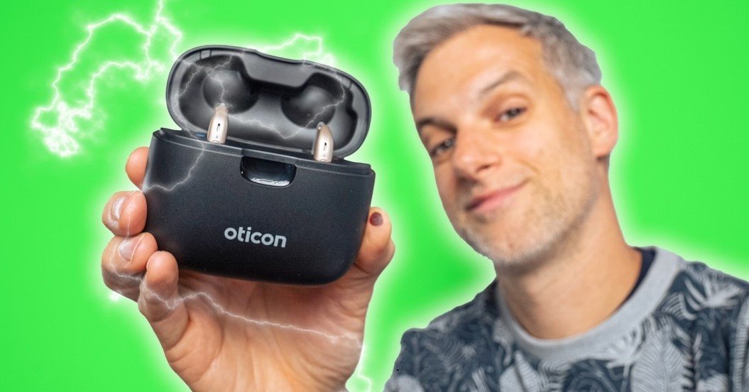 Le youtubeur Monsieur GRrr sur fond vert qui tient à la main des aides auditives Oticon More dans leur smart charger