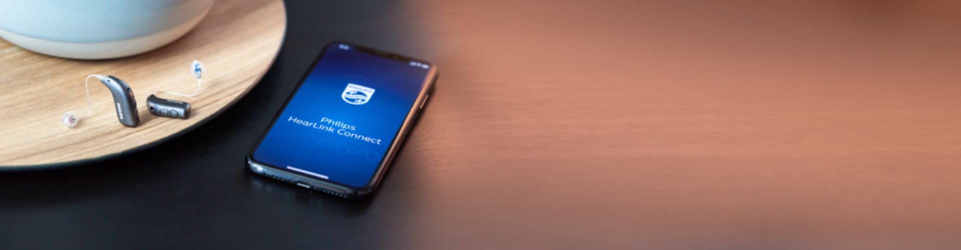 Ένα ζευγάρι βοηθήματα ακοής Philips HearLink δίπλα σε ένα smartphone με ανοιχτή την εφαρμογή Philips HearLink. 