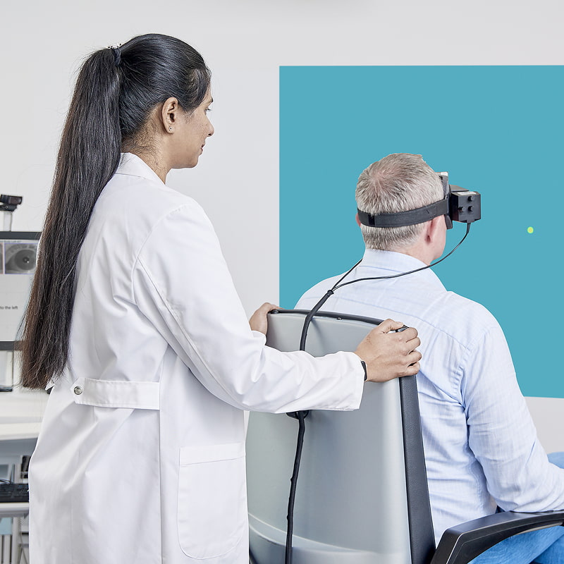 Clinicien réalisant un test cervico-oculaire sur un patient assis dans le fauteuil rotatif inclinable Orion et portant les lunettes VisualEyes VNG.