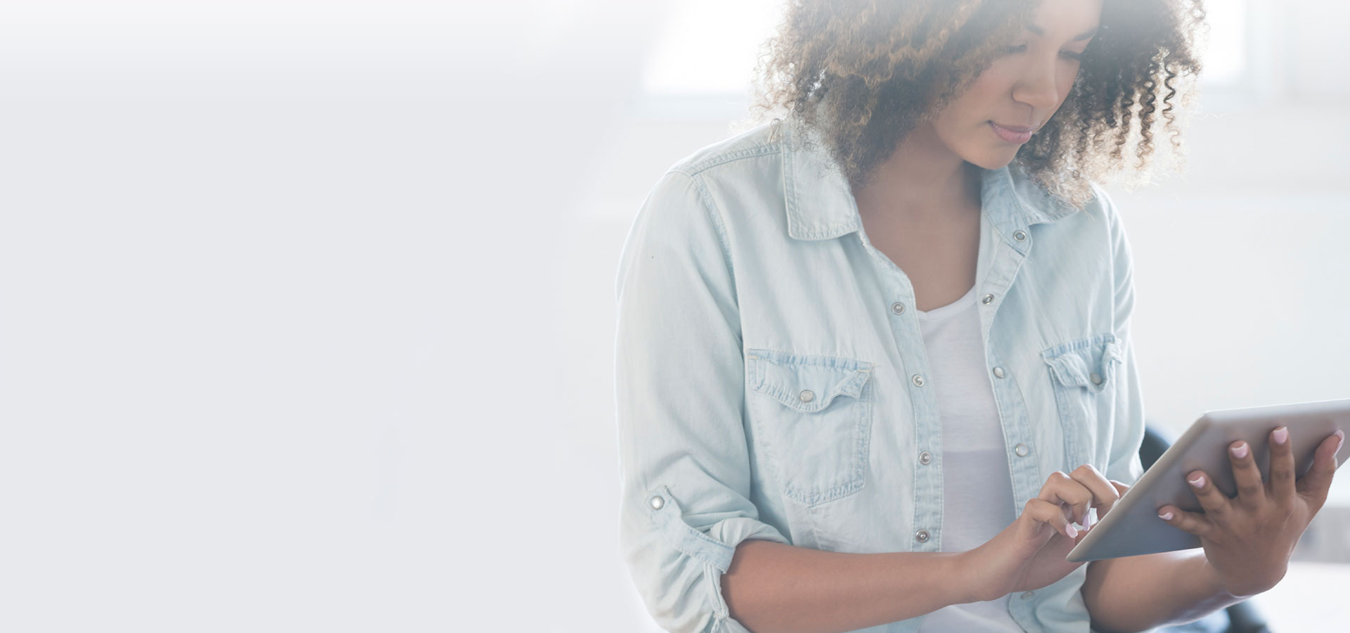 jeune femme metisse aux cheveux bouclés regarde un ipad, tablette numérique