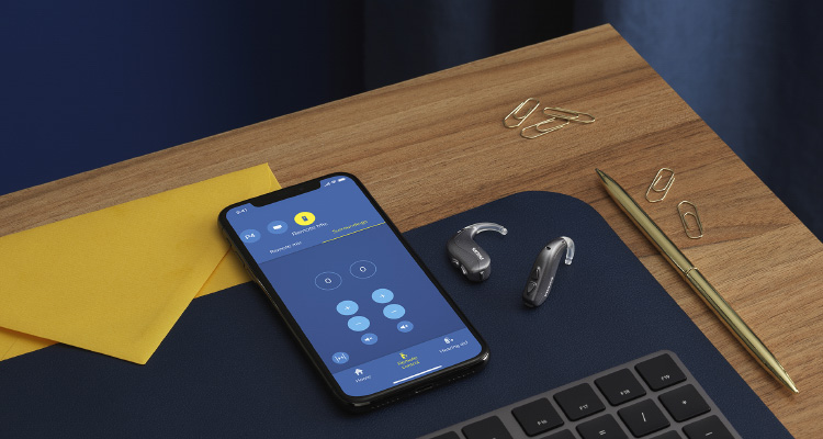 필립스 히어링크 앱이 실행된 스마트폰 옆에 필립스 히어링크 BTE PP 보청기가 있습니다.