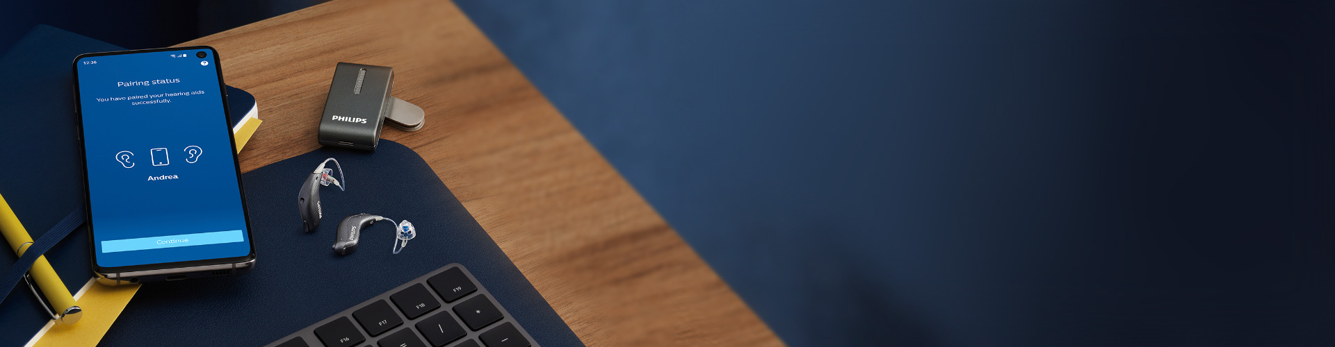 필립스 오디오클립 옆에 있는 필립스 히어링크 miniRITE 보청기와 필립스 히어링크 앱이 실행된 스마트폰.