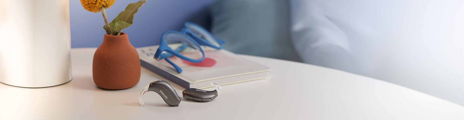 Philips HearLink hoortoestellen in de mini-achter-het-oor uitvoering (miniBTE T) op een tafel met boeken, bril, lampen en bloemen