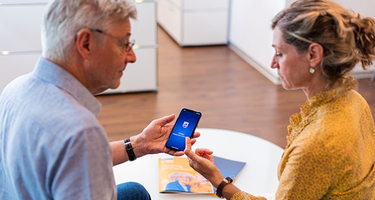 Man met Philips HearLink hoortoestellen in een counselingsessie met een vrouwelijke audicien, die de Philips HearLink app leert gebruiken