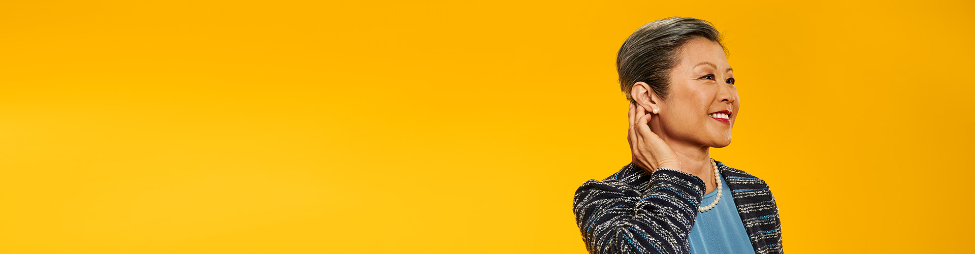 女士配戴著飛利浦助聽器,微笑著碰觸可以幫助她聆聽更好的助聽器.